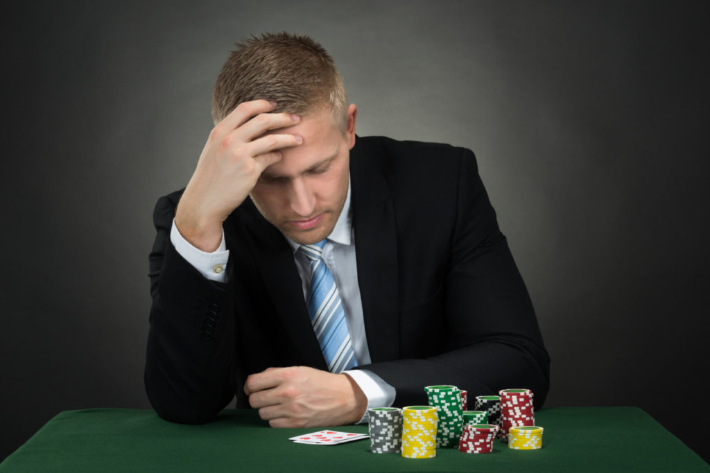 Nedtrykt mand ved pokerbord - gambling og ludomani